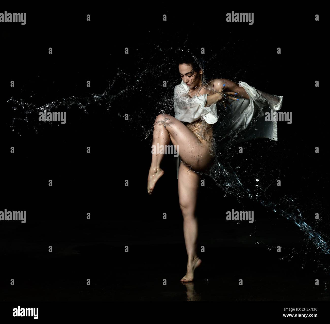 Young beautiful woman of Caucasian appearance with long black hair is dancing in a white shirt in the rain on a black background Stock Photo