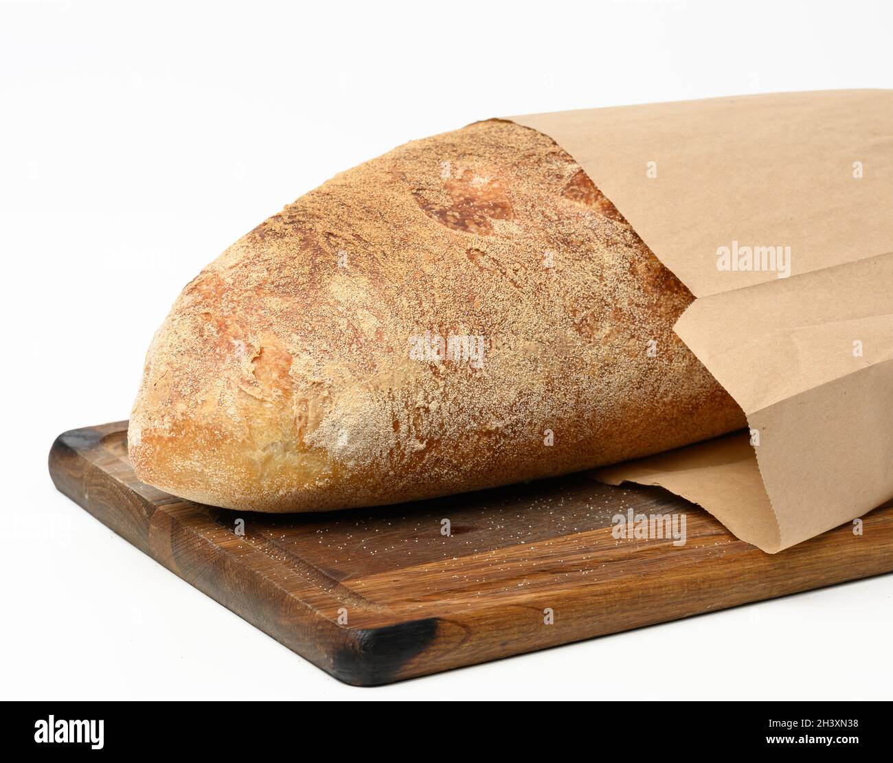 Whole baked oval bread made from white wheat flour in a paper bag on a wooden board Stock Photo