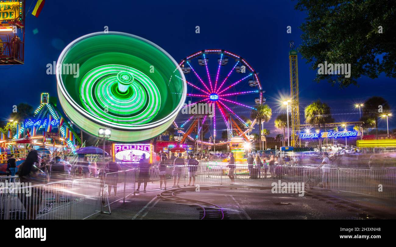 wide view of several rides at a traveling amusement park and concession stands with a long exposure and all the rides in motion at night Stock Photo