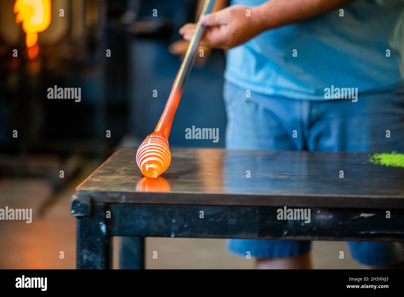 a worker is in the process of creating a glass vase and is rolling