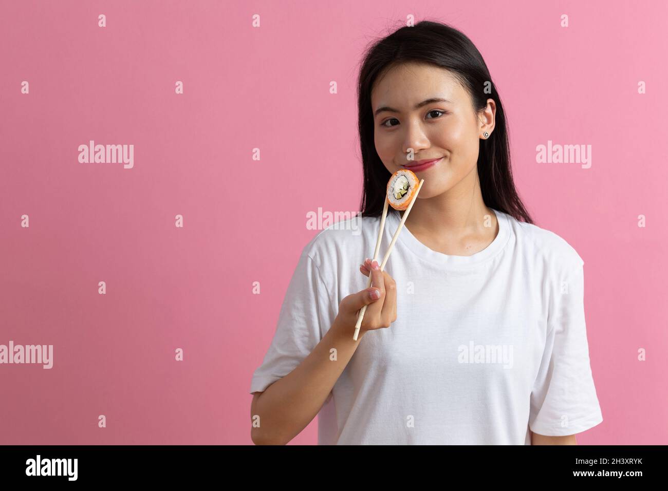 Asian beauty model girl eating Sushi roll, healthy japanese food. Beautiful woman holding chopsticks with Philadelfia roll Stock Photo