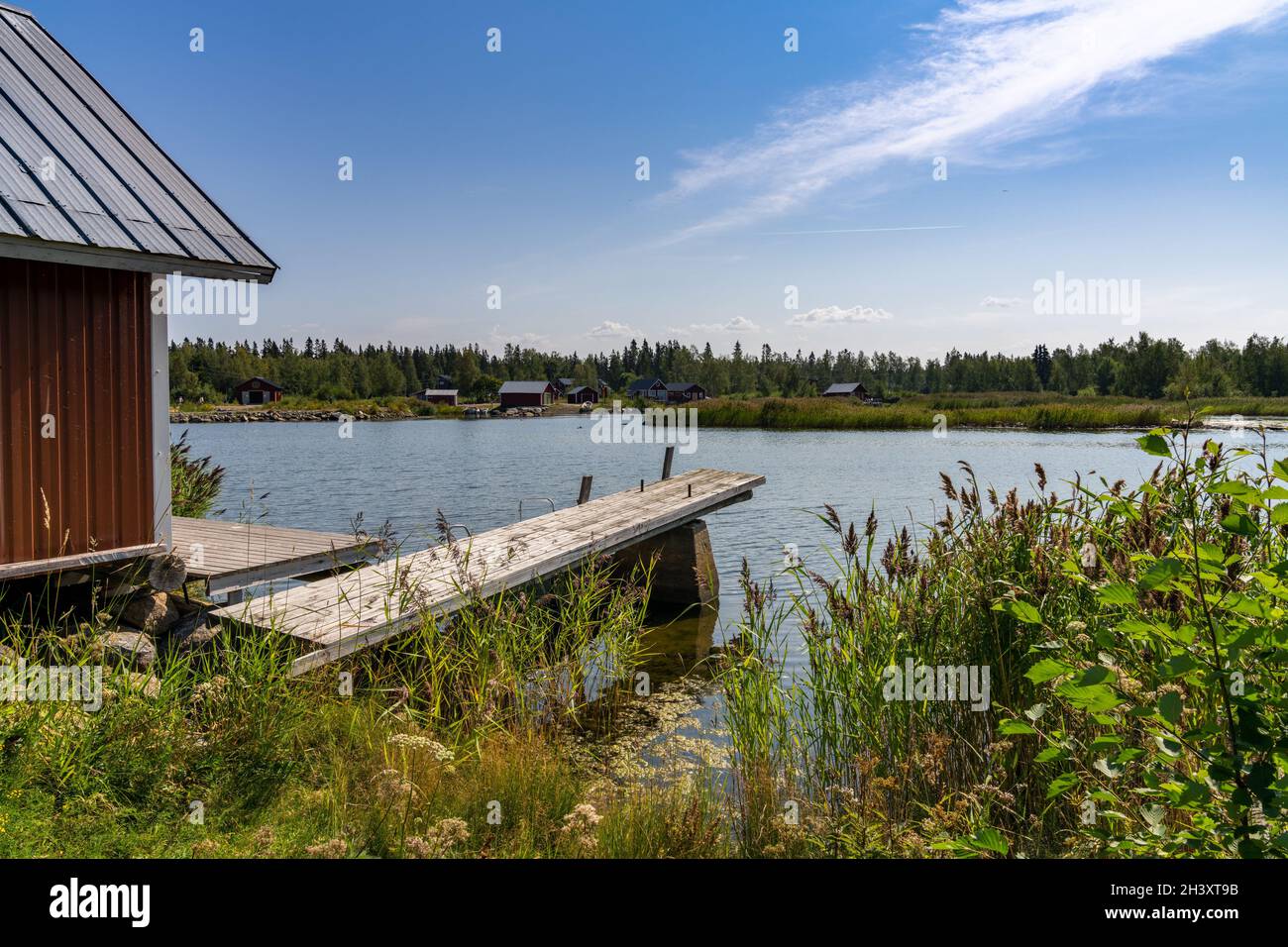 An idyllic lake landscape with a wooden cottage and a wooden dock on a beautiful summer day Stock Photo