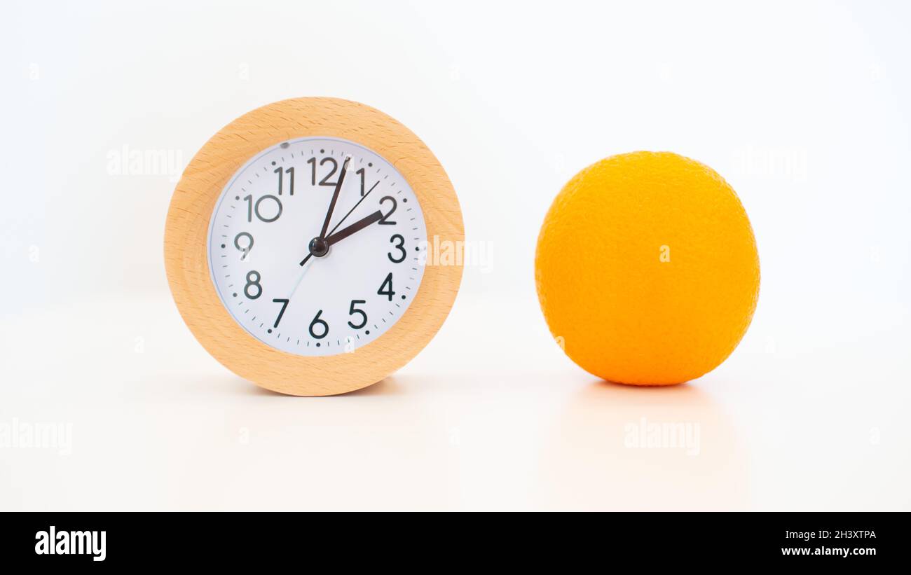 Alarm clock and orange fruit in hand on white table background Stock Photo