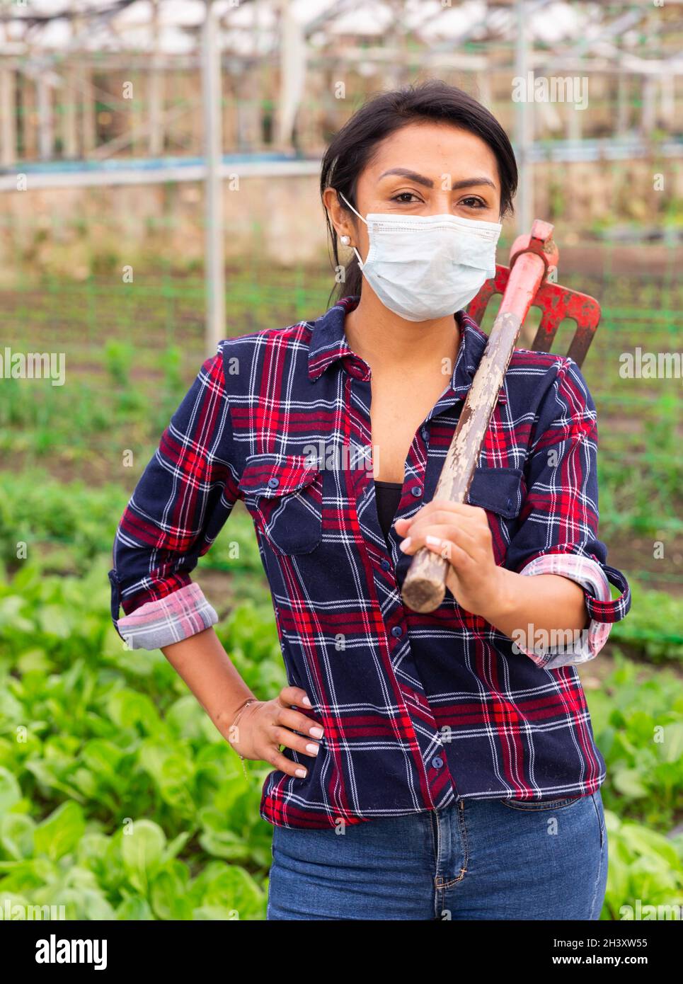 Portrait of a hispanic female farmer with a rake in a greenhouse ...