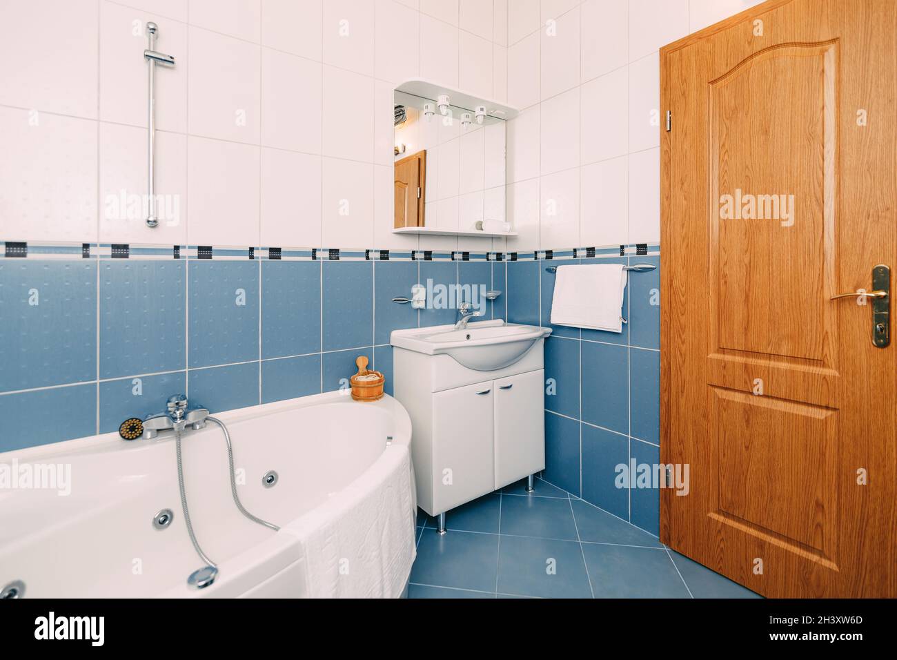 Bathroom with hydromassage bathtub, washbasin with mirror and brown wooden door. Stock Photo