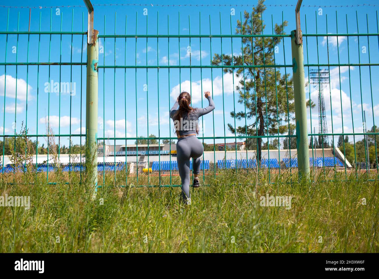 Girl climb the fence of stadium. Young sport woman going to run