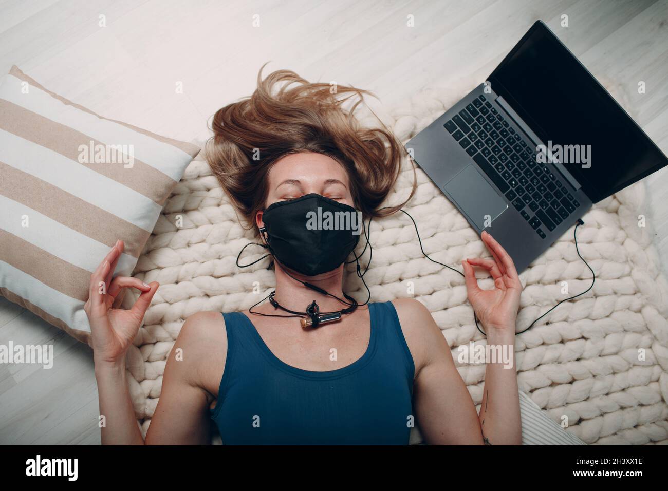 Adult mature woman doing yoga nidra and lay in face mask at home living room with online tutorials on laptop Stock Photo