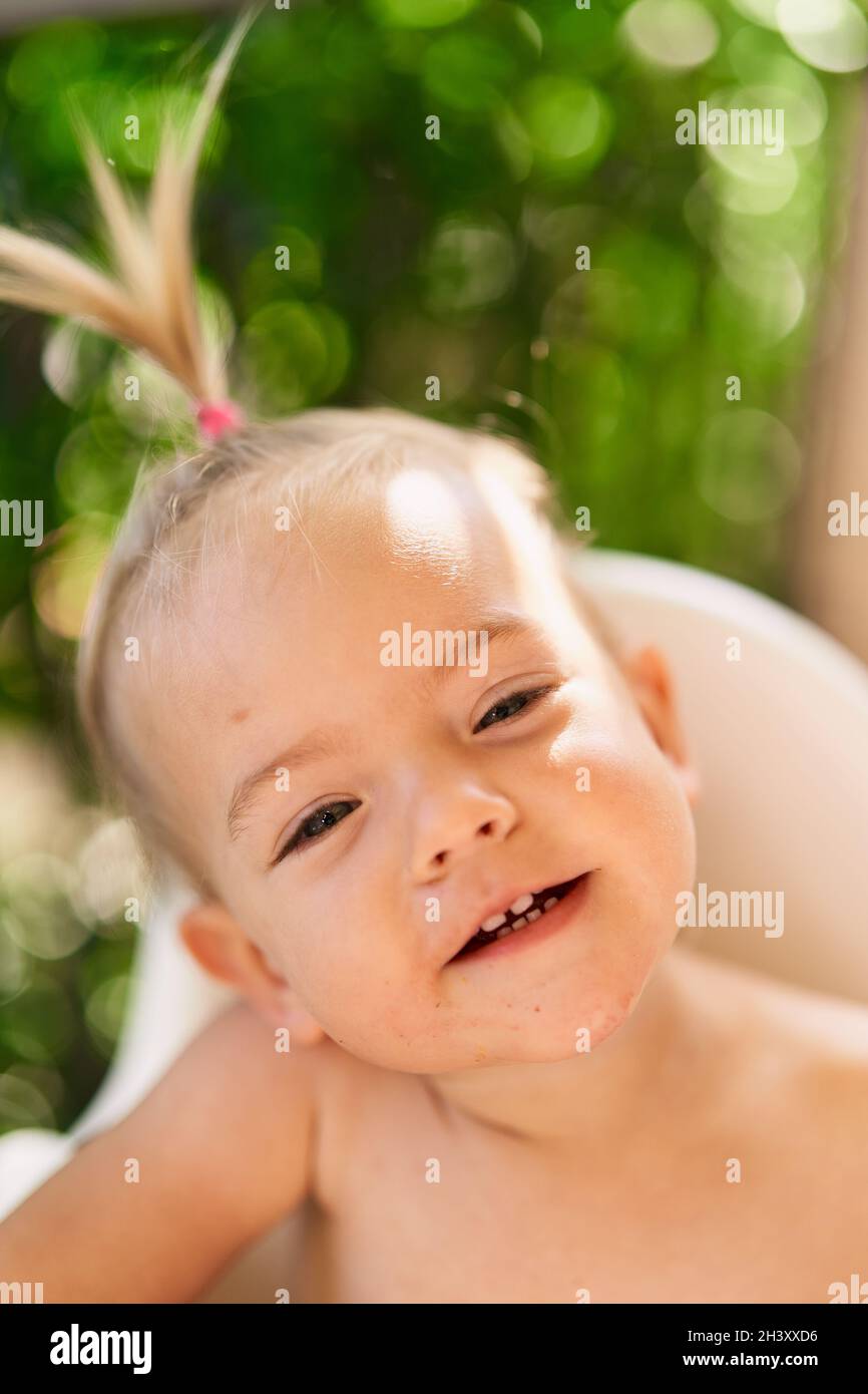 Smiling little girl with a ponytail sits on a high chair. Portrait Stock Photo