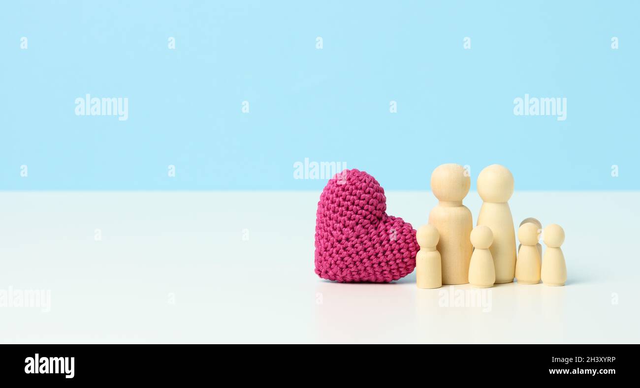 Red knitted heart and wooden figurines family on a blue background. The concept of cohesion and love in the family, love for chi Stock Photo