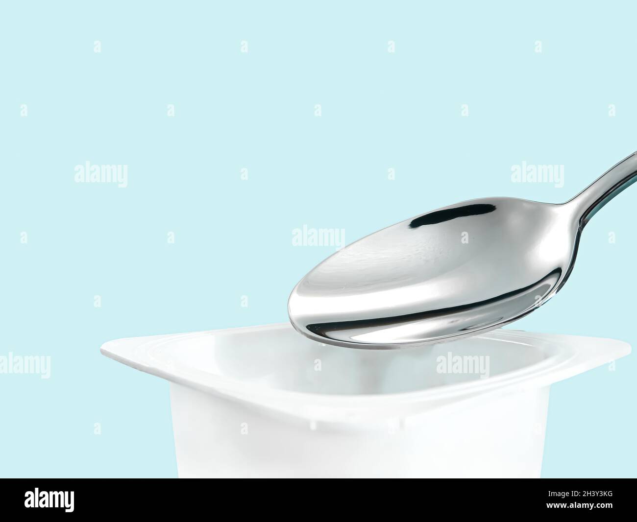 Yogurt cup and silver spoon on mint background, white plastic container
