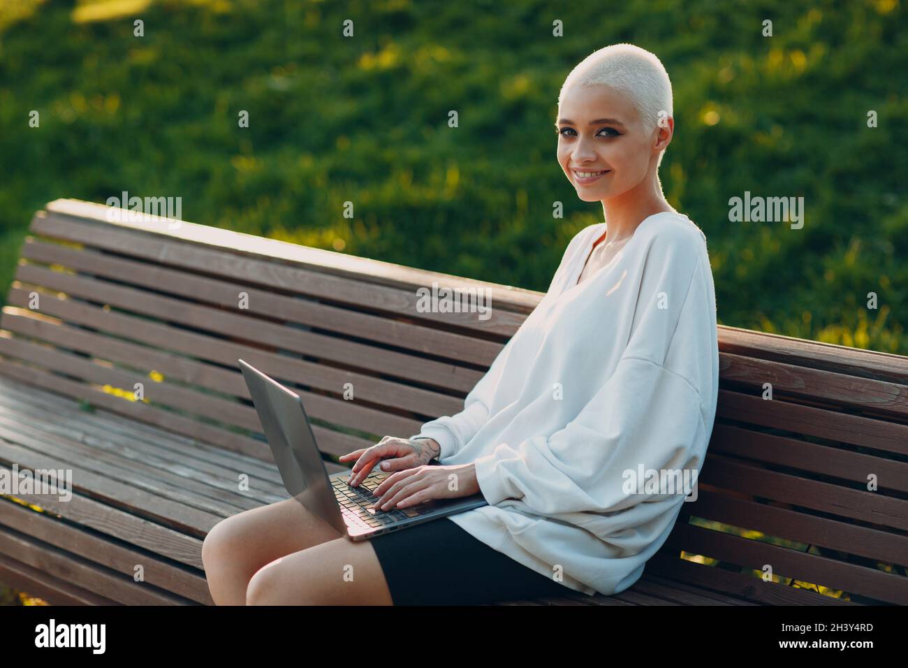 Millenial young woman blonde short hair outdoor smiling portrait with laptop. Stock Photo
