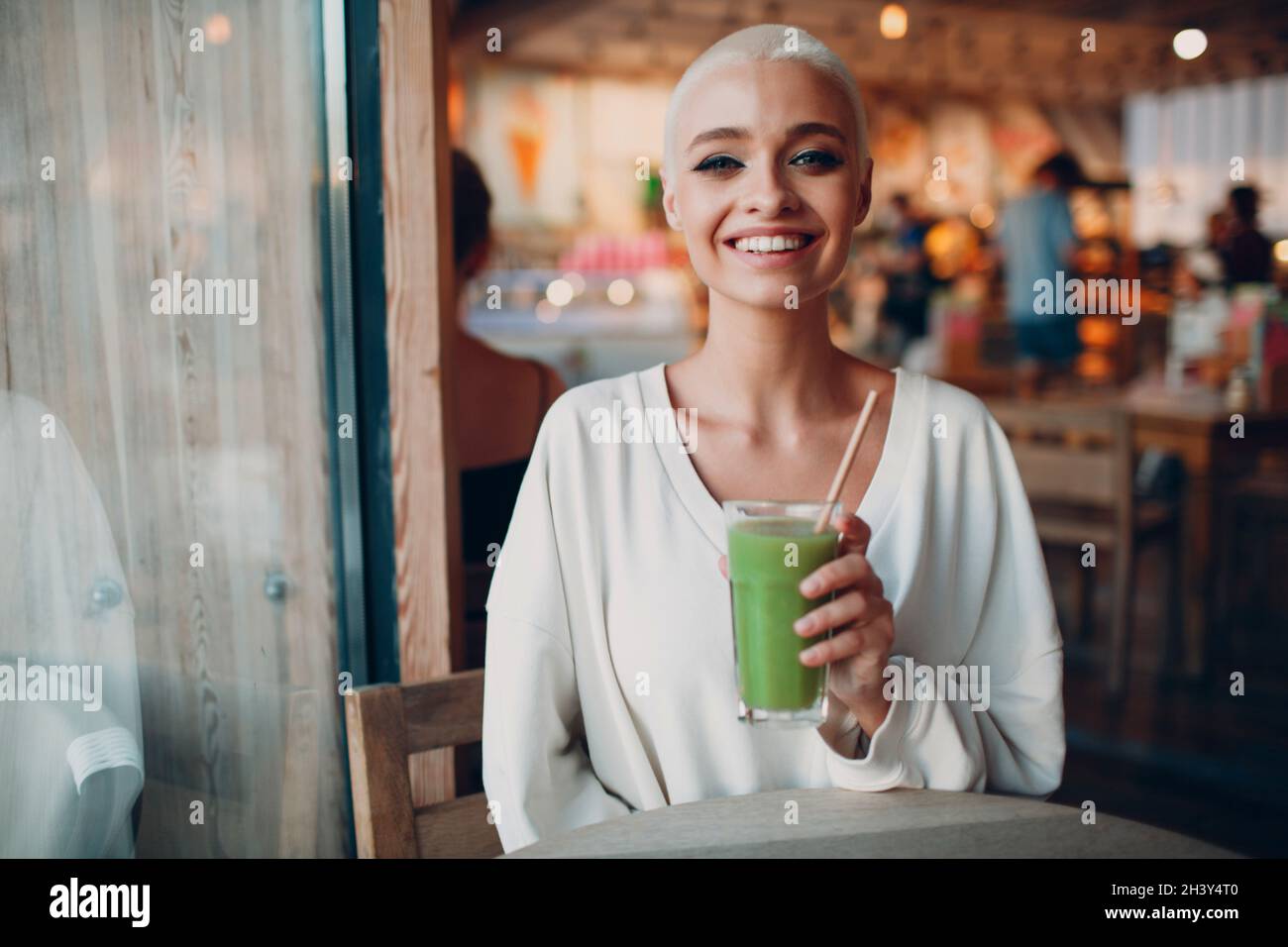 Millenial young woman blonde short hair indoor with green smoothie Stock Photo