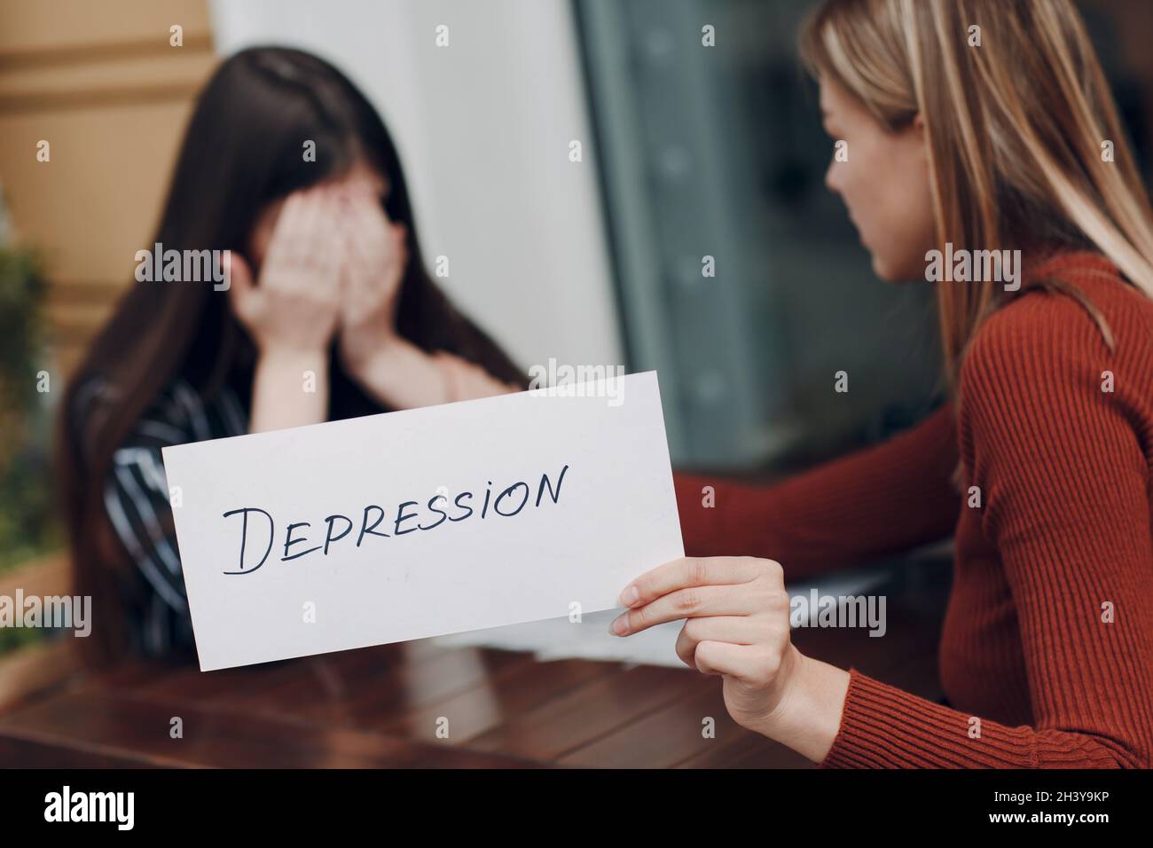 Hidden depression and stress concept. Woman crying. Second woman holding white sheet paper labeled word Depression in hand Stock Photo