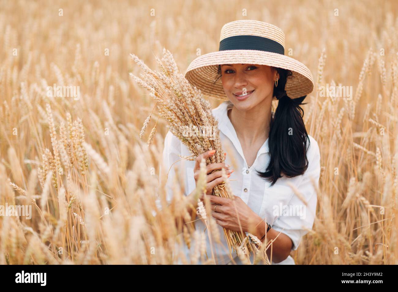 Young Woman in straw hat holding sheaf of wheat ears at agricultural ...