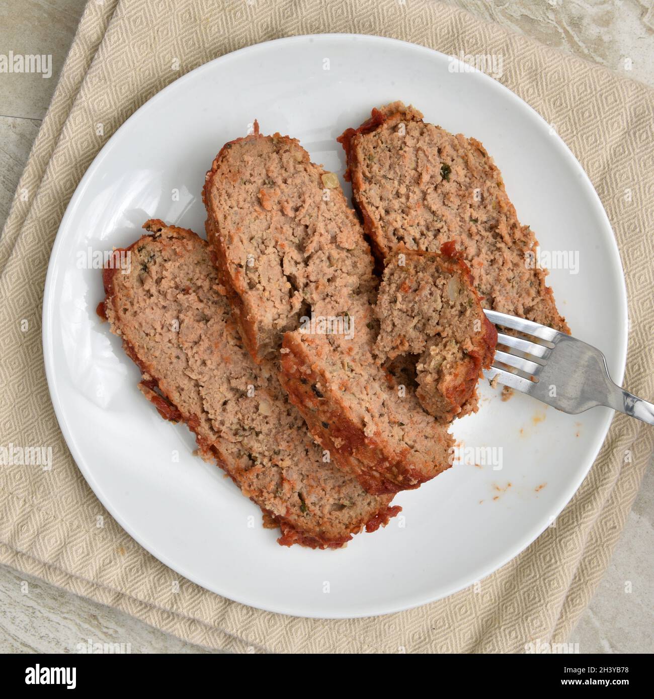 Fork taking a bite of fresh, hot sliced meatloaf on a plate, overhead view Stock Photo