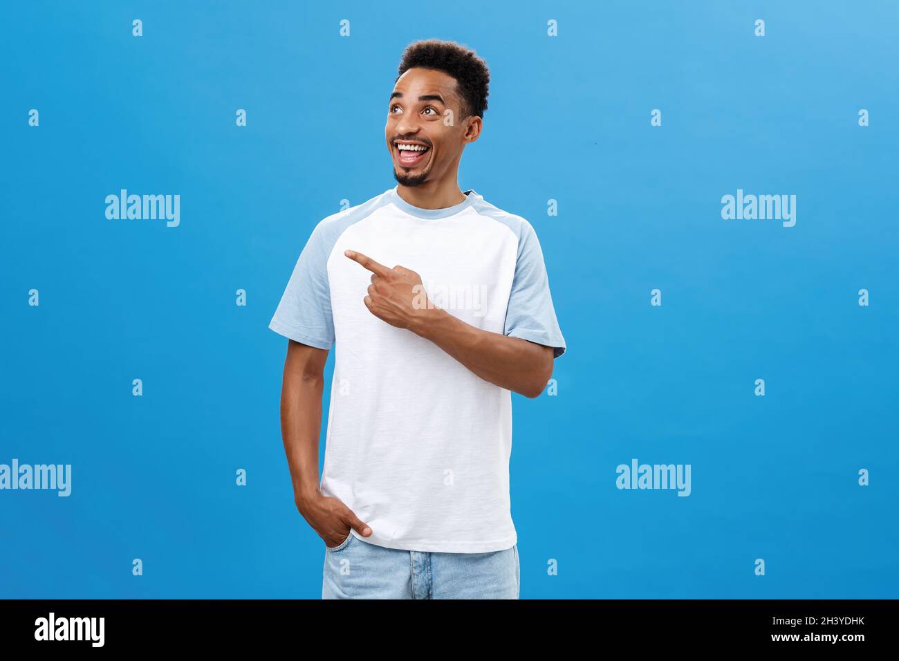 Studio shot of friendly joyful and emotive handsome dark-skinned bearded guy with afro haircut pointing and looking left with ex Stock Photo