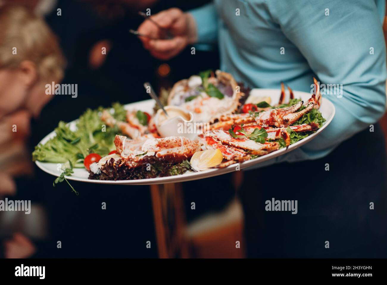A waiter in a restaurant holds seafood dishes and serves a table catering Concept Healthy food octopus and crabs shellfish Stock Photo