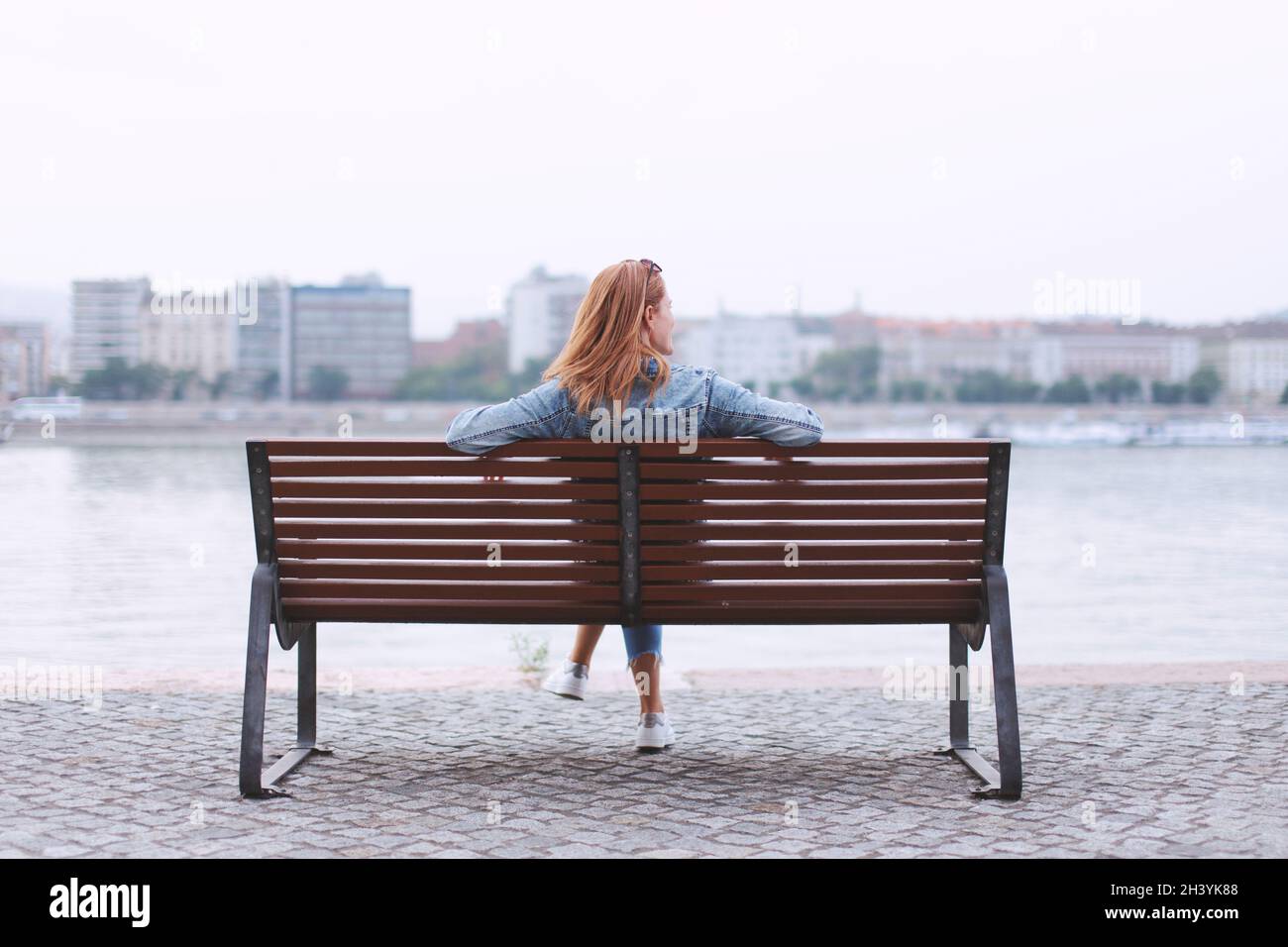 Young redhead woman relaxing on bench at riverside Stock Photo