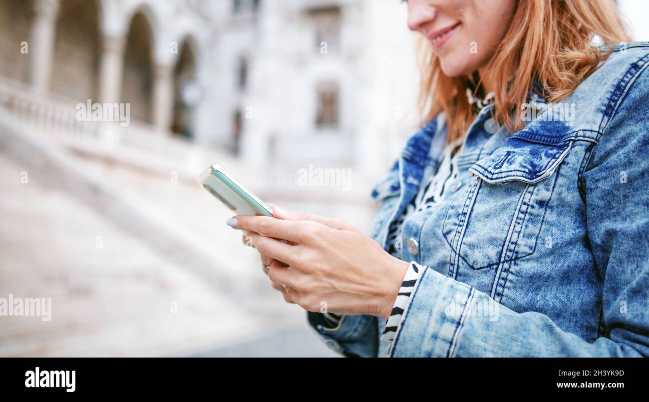 Young redhead Caucasian woman messaging on smartphone in city closeup Stock Photo