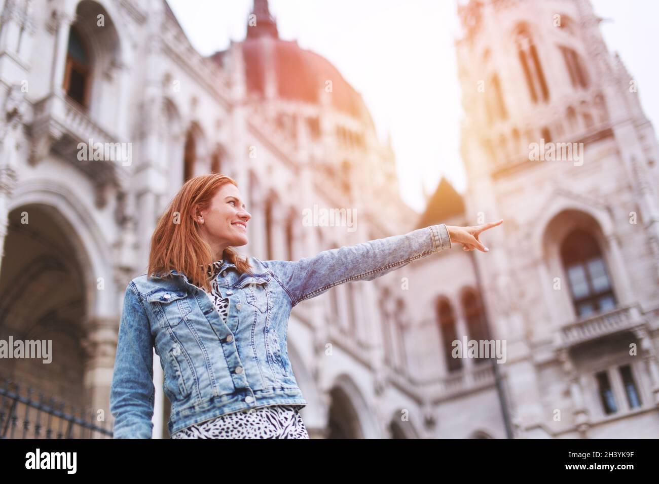 Young redhead Hungarian woman pointing at Hungarian Parliament building at Budapest, Hungary Stock Photo