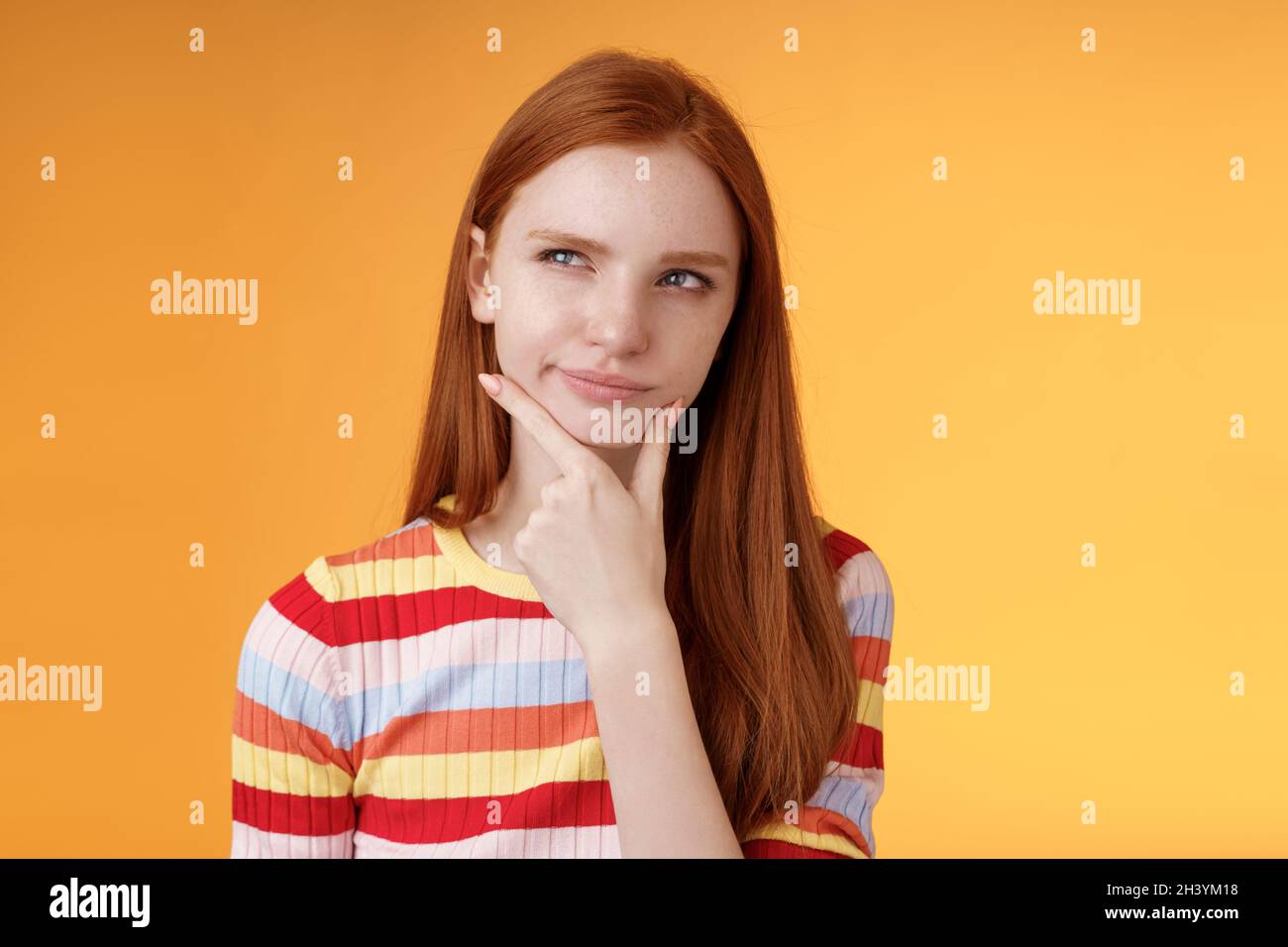 Hmm interesting. Suspicious doubtful attractive european redhead female pondering choice look hesitant thoughtful touch chin smi Stock Photo