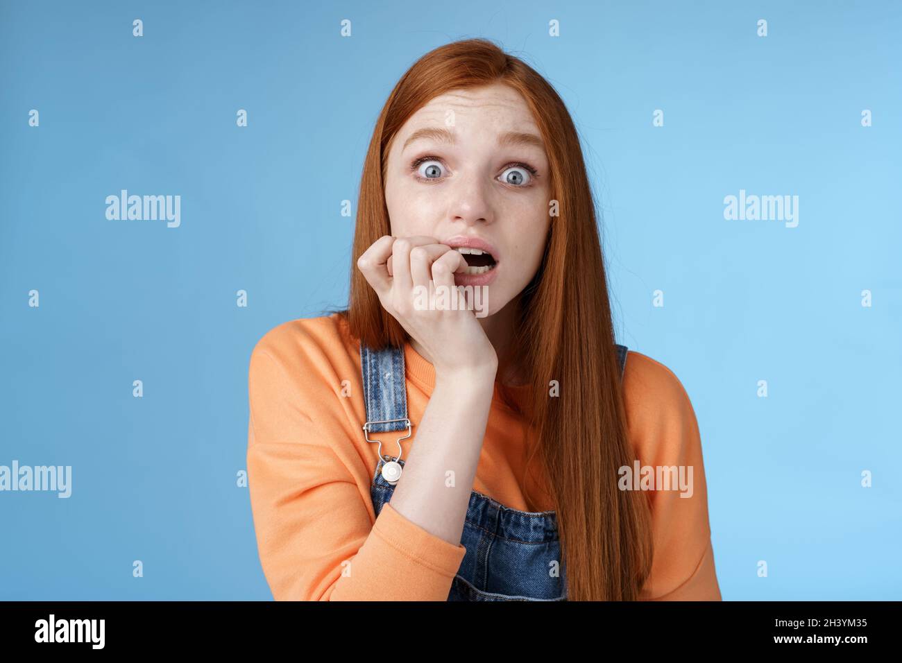 Scared unconfident anxious young trembling redhead girl wide eyes staring intense emotional biting fingernails, fan worry favori Stock Photo