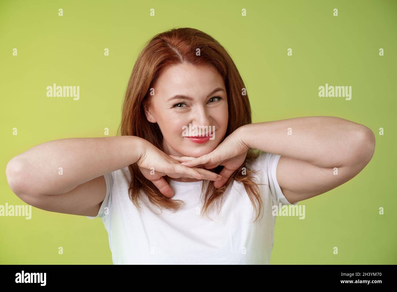 Aging, cosmetology, wellbeing concept. Happy self-assured redhead woman hold hands under jawline smiling showing facial blemishe Stock Photo
