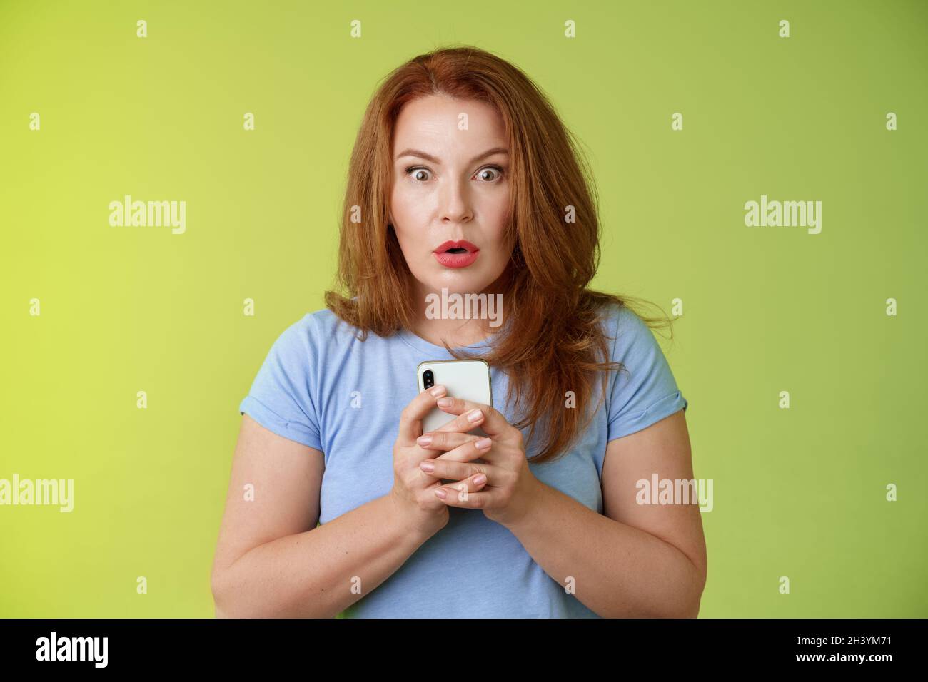 Shocked speechless impressed redhead european middle-aged woman fold lips astonished wow stare camera fascinated react amazed wo Stock Photo