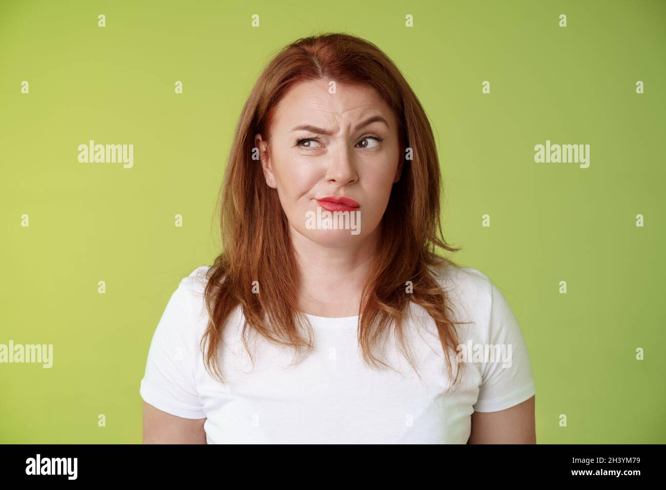 Perplexed doubtful unsure redhead wife smirking unsatisfied frowning look aside displeased disappointed hesitating pondering str Stock Photo