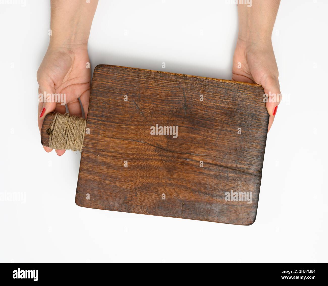 Female hands hold empty rectangular brown wooden chopping board isolated on white background Stock Photo
