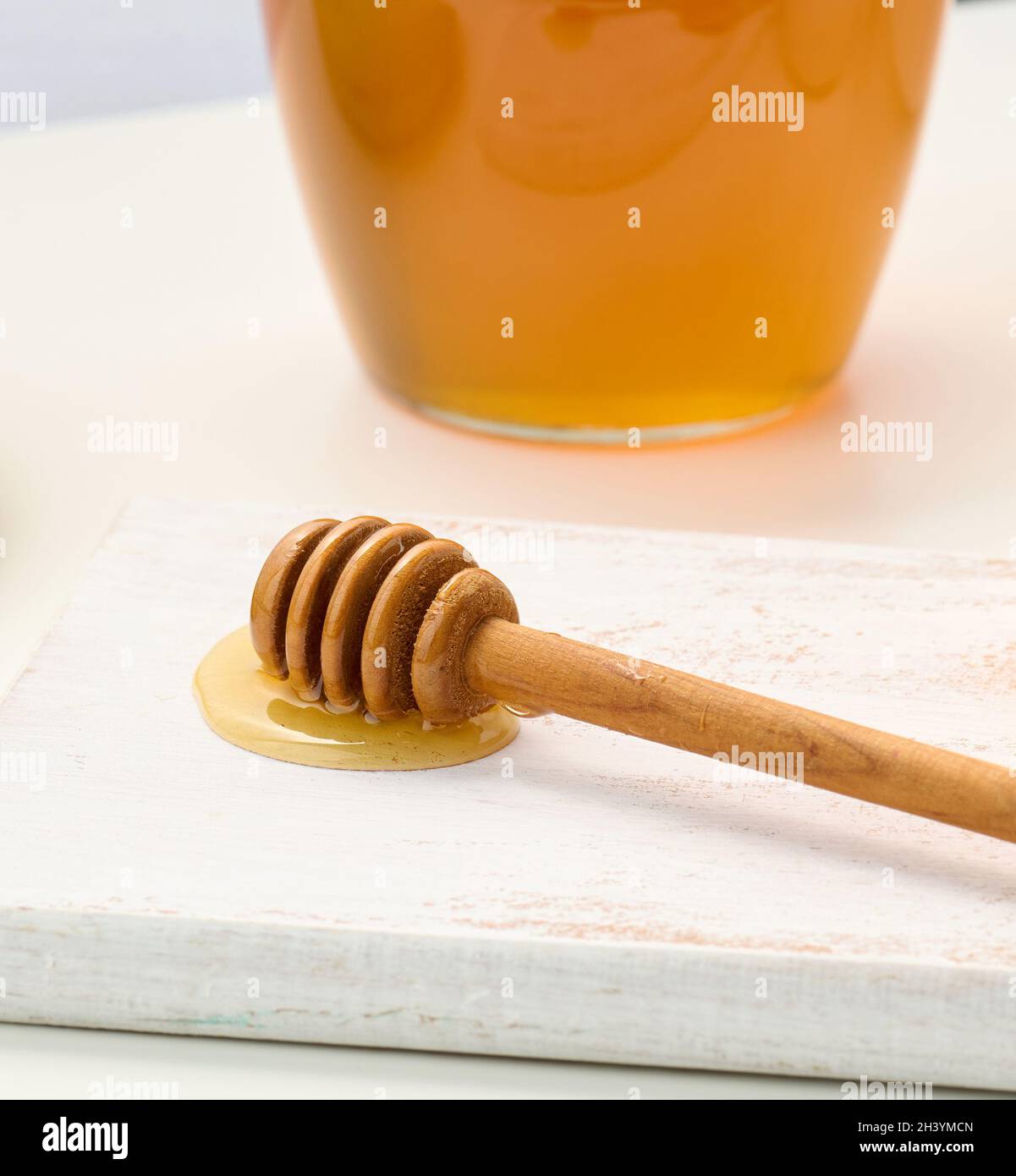 Honey in a glass transparent jar and a wooden stick on a white table Stock Photo