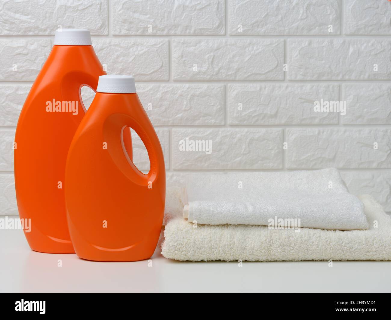 Two orange plastic bottles of liquid detergent and a stack of towels on a white shelf, home wash Stock Photo