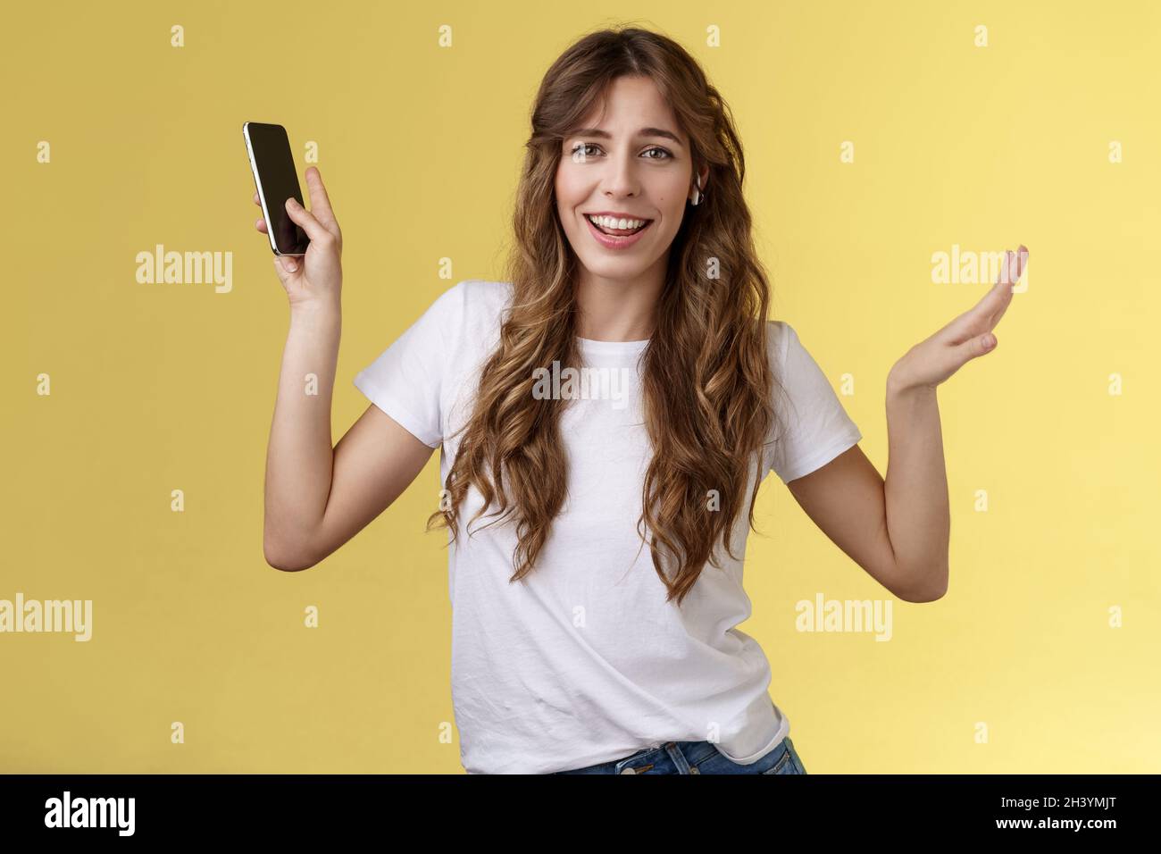 Carefree good-looking lively sociable curly-haired girl having fun wearing wireless earbuds dancing joyfully listening music mov Stock Photo