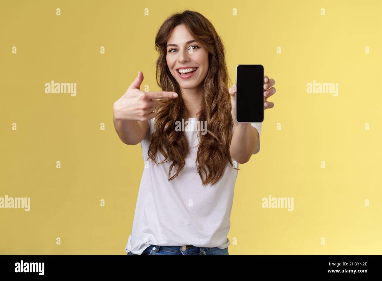 Cheerful sassy good-looking sociable girl curly long hair extend arm holding smartphone pointing index finger mobile phone scree Stock Photo