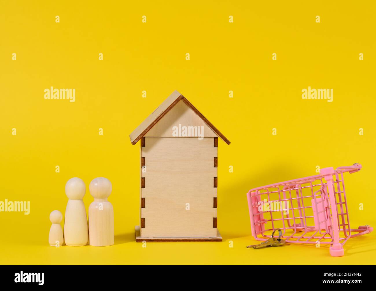 Wooden house and metal miniature cart on a yellow background. Real estate purchase concept Stock Photo