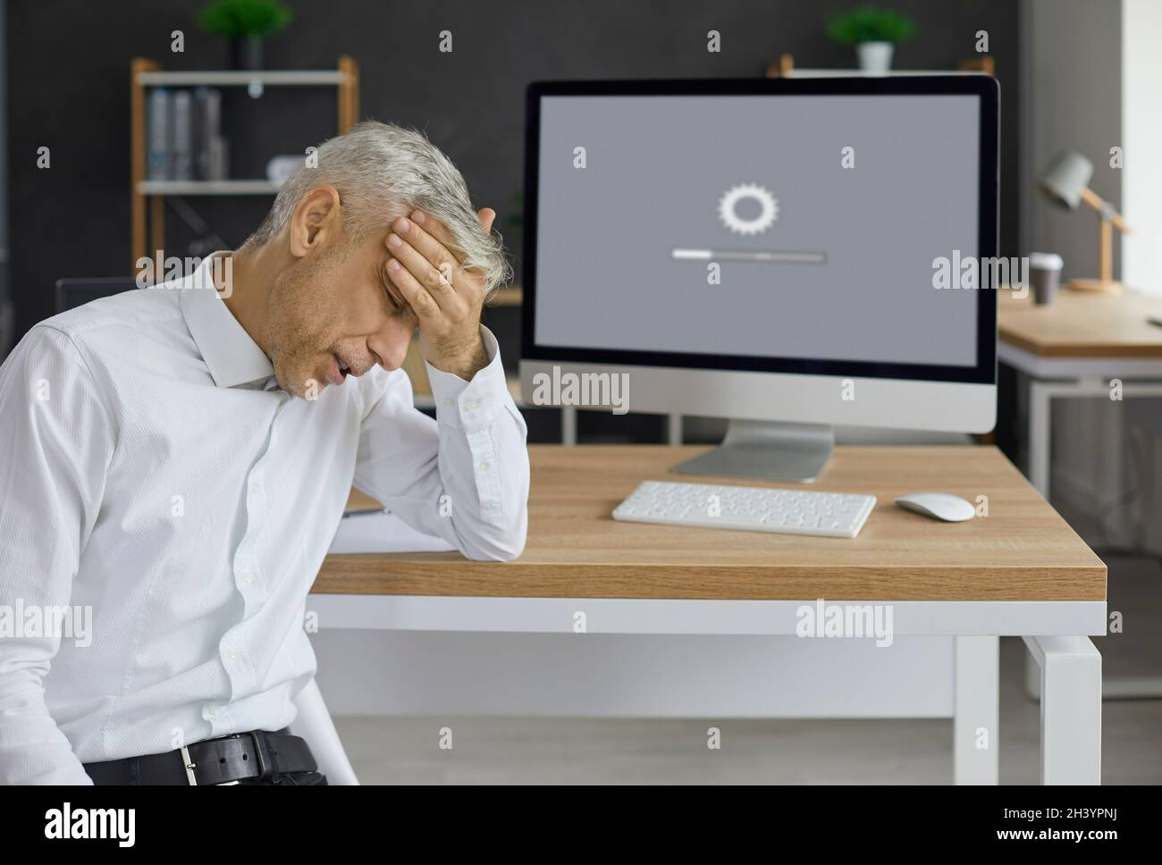 Office worker sitting in front of desktop computer and waiting for system to load Stock Photo