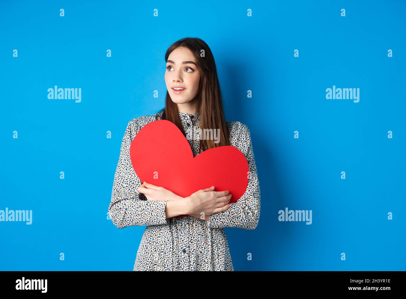 Valentines day. Hopeful girl dreaming off soulmate, looking aside at empty space with excitement, hugging big red heart cutout, Stock Photo