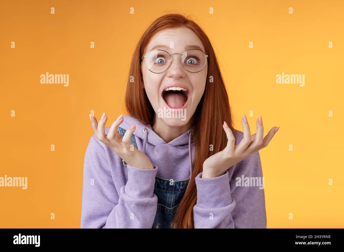 Shocked excited overwhelmed young screaming happy redhead girl wearing glasses winning hear excellent news yelling out loud rejo Stock Photo