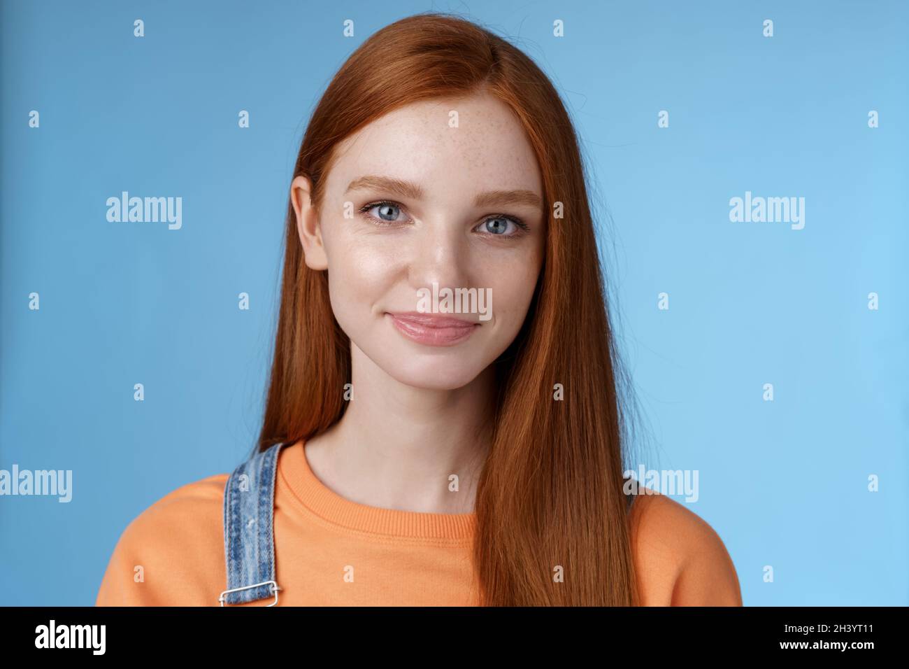 Outgoing young redhead girl blue eyes wearing orange t-shirt overalls smiling pleasantly casually talking standing good mood joy Stock Photo