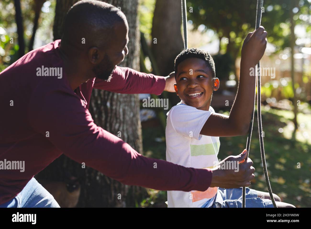 African american father with son having fun and playing on swing in ...