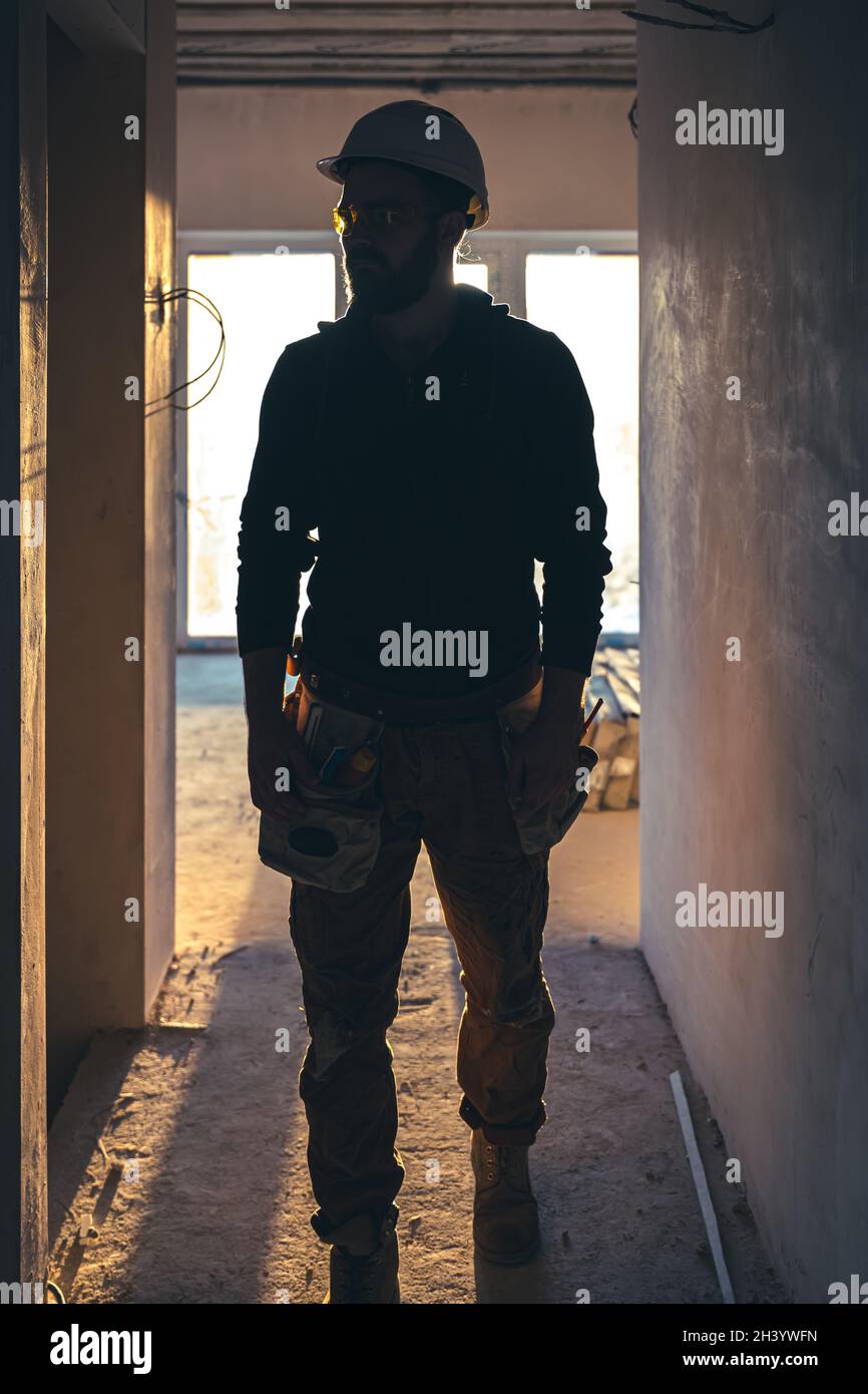 A man builder in work clothes with a protective helmet at a construction site. Stock Photo