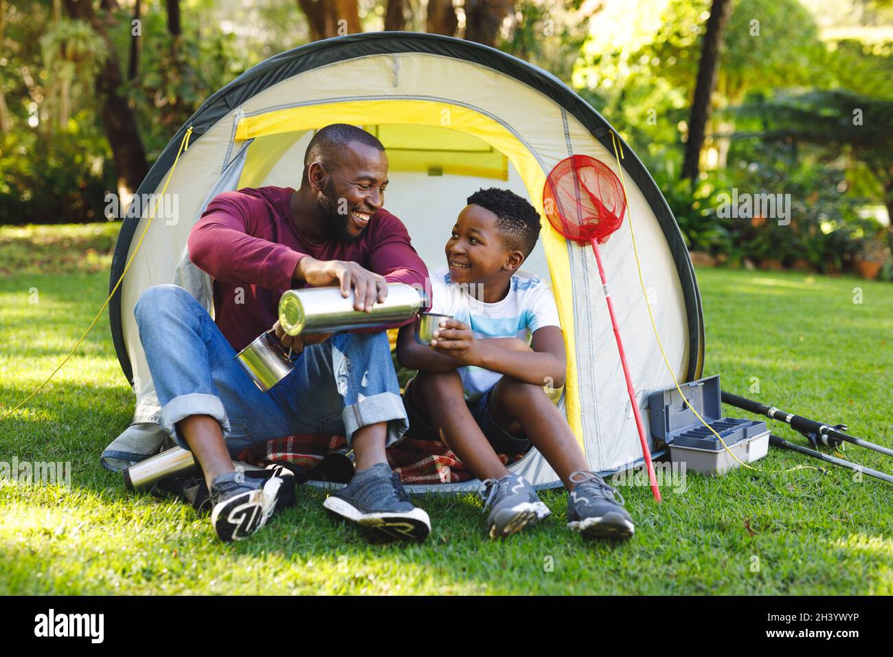 African american father with son having fun and sitting in tent pouring ...