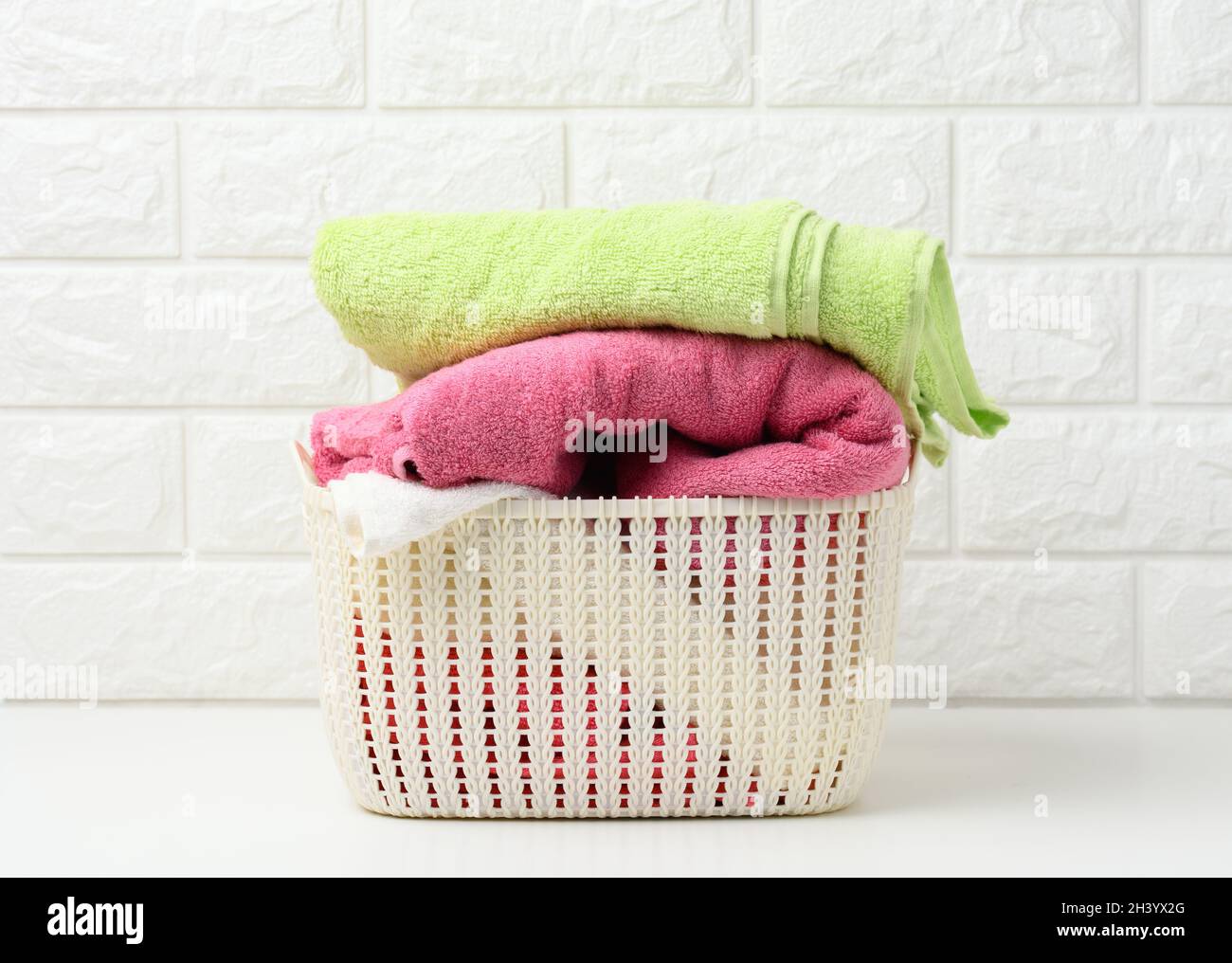 Clean rolled terry towels in a plastic basket on a white shelf, bathroom interior Stock Photo