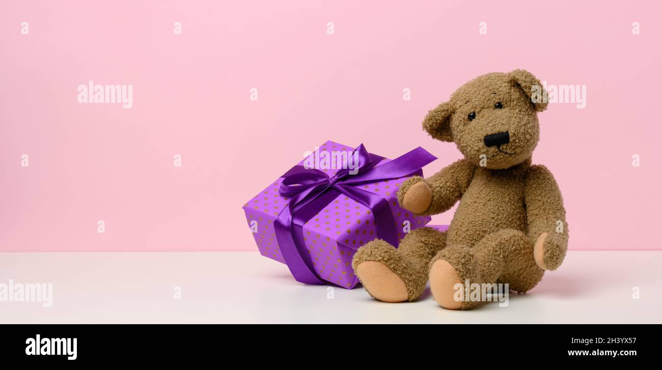 Cute brown teddy bear holding a box wrapped in paper and red silk ...