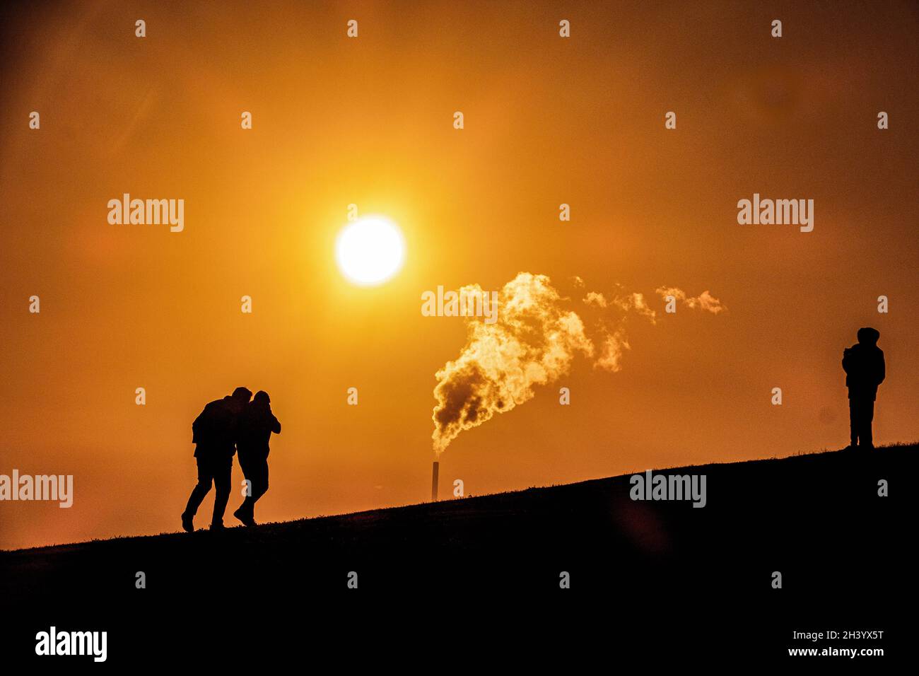 Global warming: A warming sun and steam rises as silhouettes of people stand on a hill in Melbourne Australia . Stock Photo