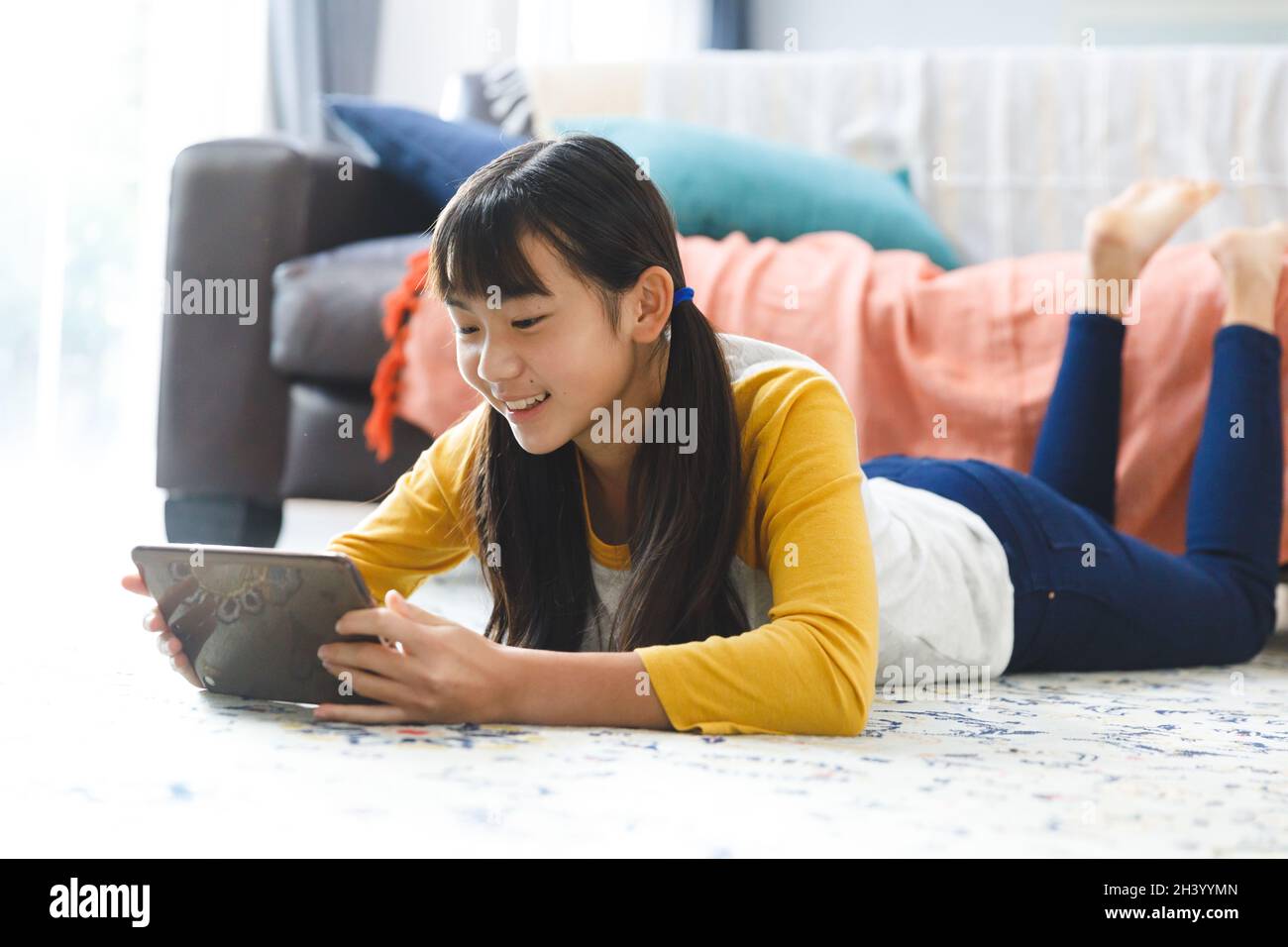Smiling asian girl lying in living room and using tablet Stock Photo ...