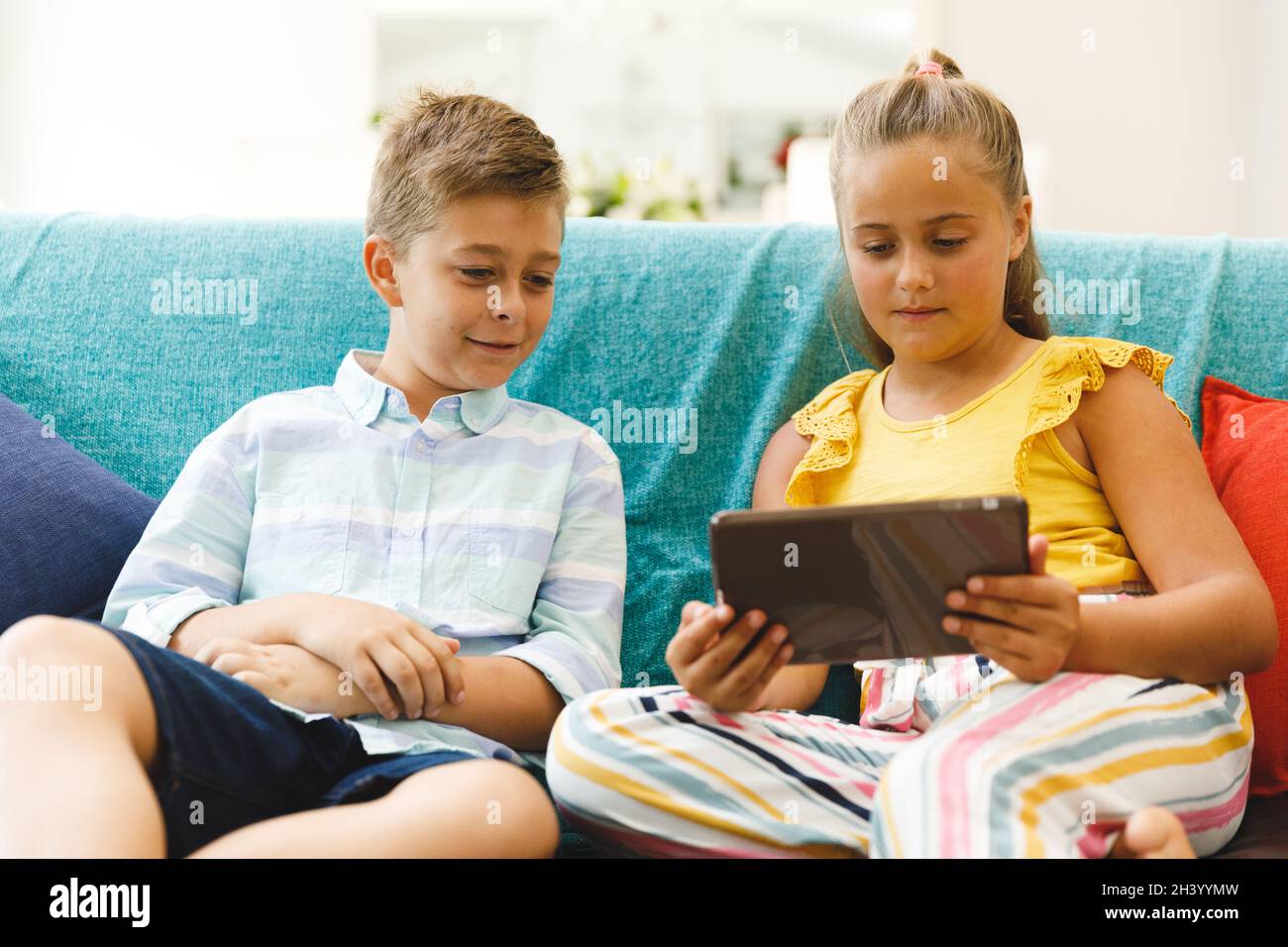 Happy caucasian brother and sister sitting on couch and using tablet in ...