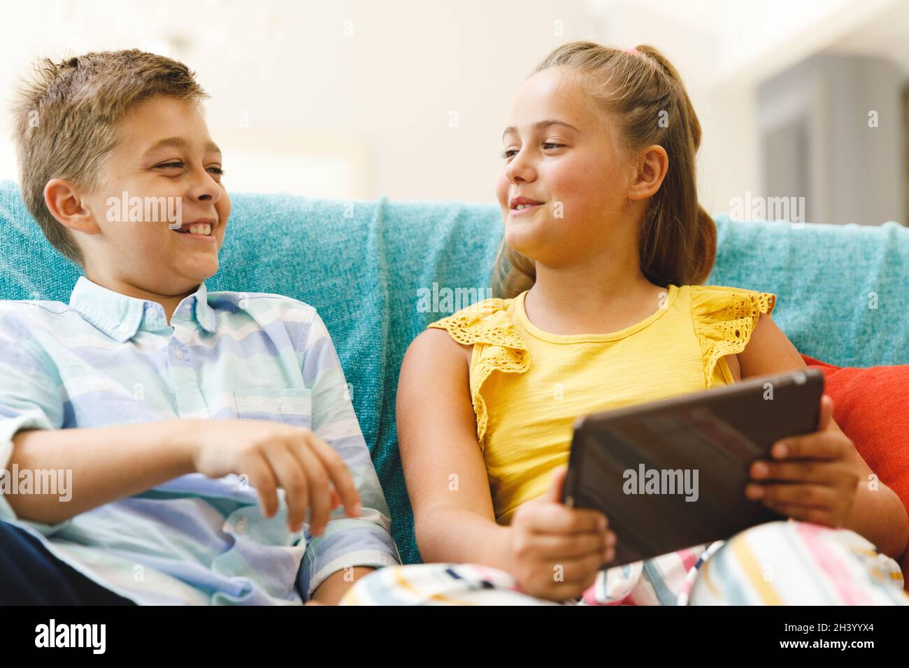 Happy caucasian brother and sister sitting on couch and using tablet in ...