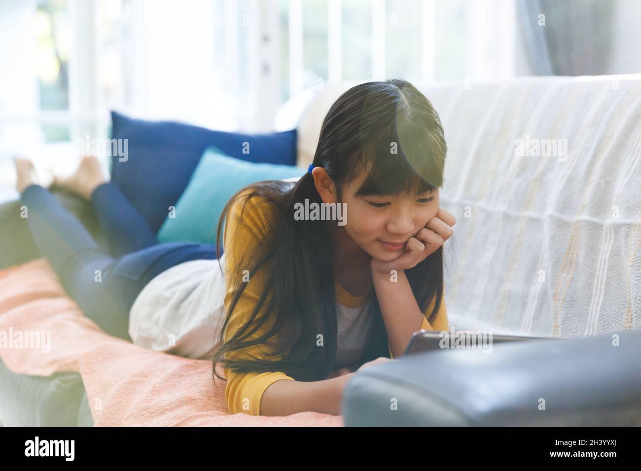 Smiling asian girl lying on couch in living room and using tablet Stock ...