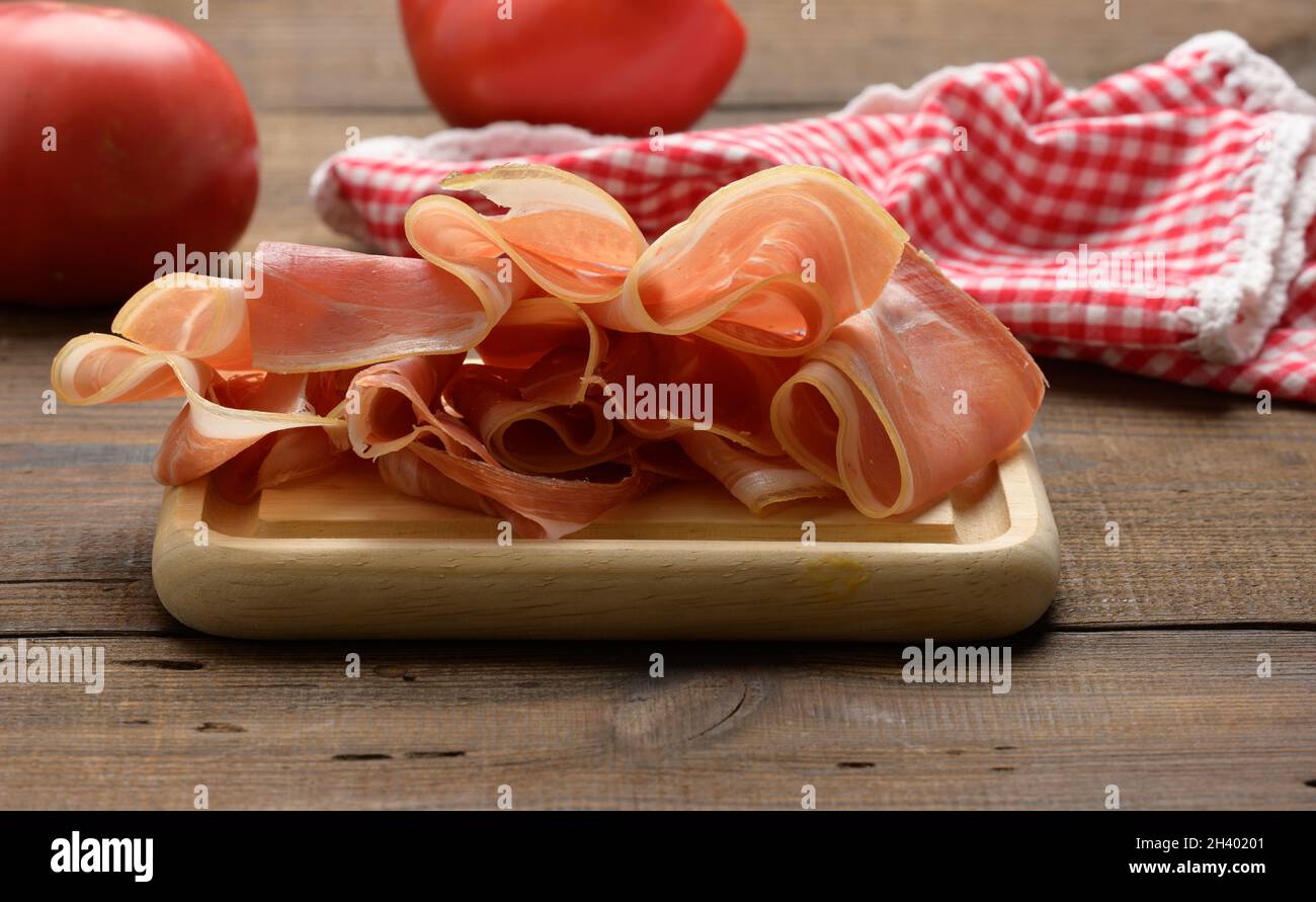 Sliced thin slices of prosciutto on wooden brown board, wooden table background Stock Photo